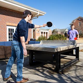 Two students playing ping-pong outside. 